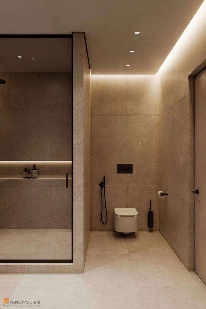 Modern minimalist beige tiled bathroom with walk-in glass shower, wall-mounted toilet, black fixtures and soft recessed LED cove lighting.