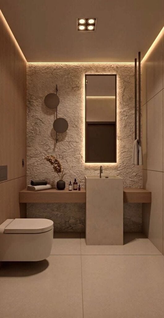 Modern minimalist bathroom with backlit mirror, textured stone wall, floating vanity and freestanding basin, warm ambient LED lighting.
