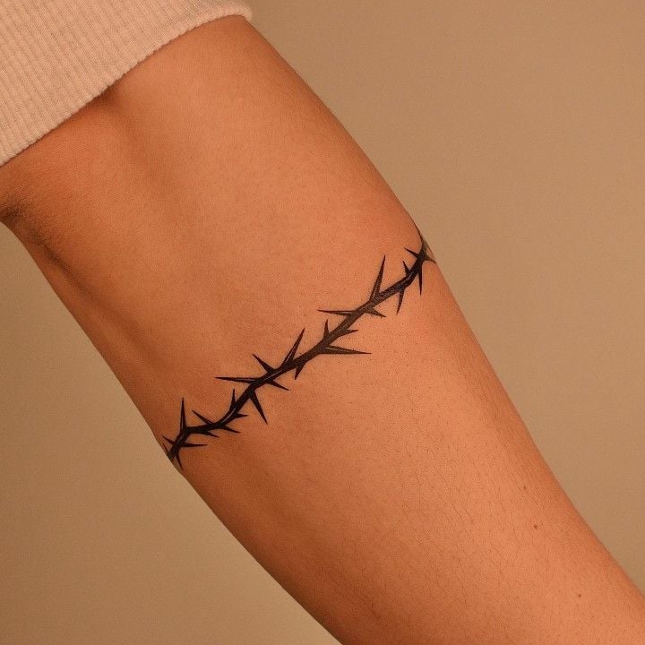 Close-up of a minimalist black thorn armband tattoo wrapped around the upper arm against a neutral background