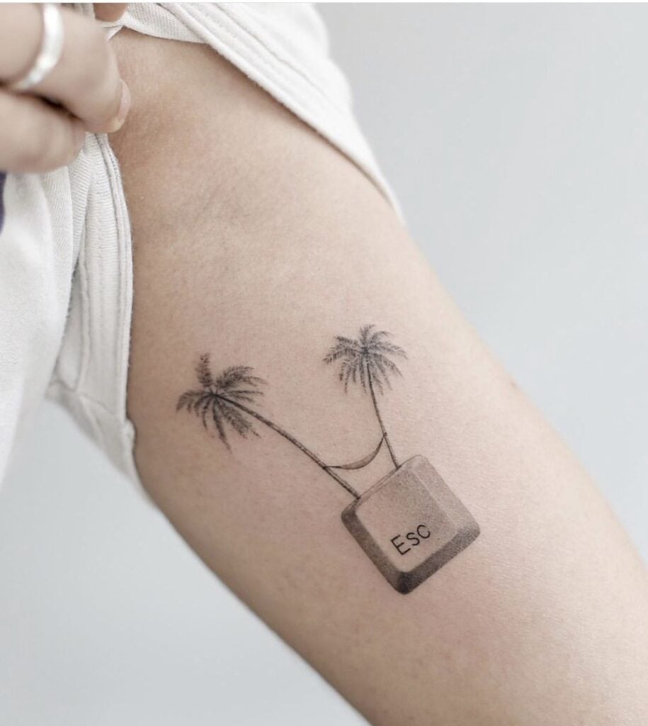 Minimalist black-ink arm tattoo showing an Esc computer key used as a hammock strung between two palm trees