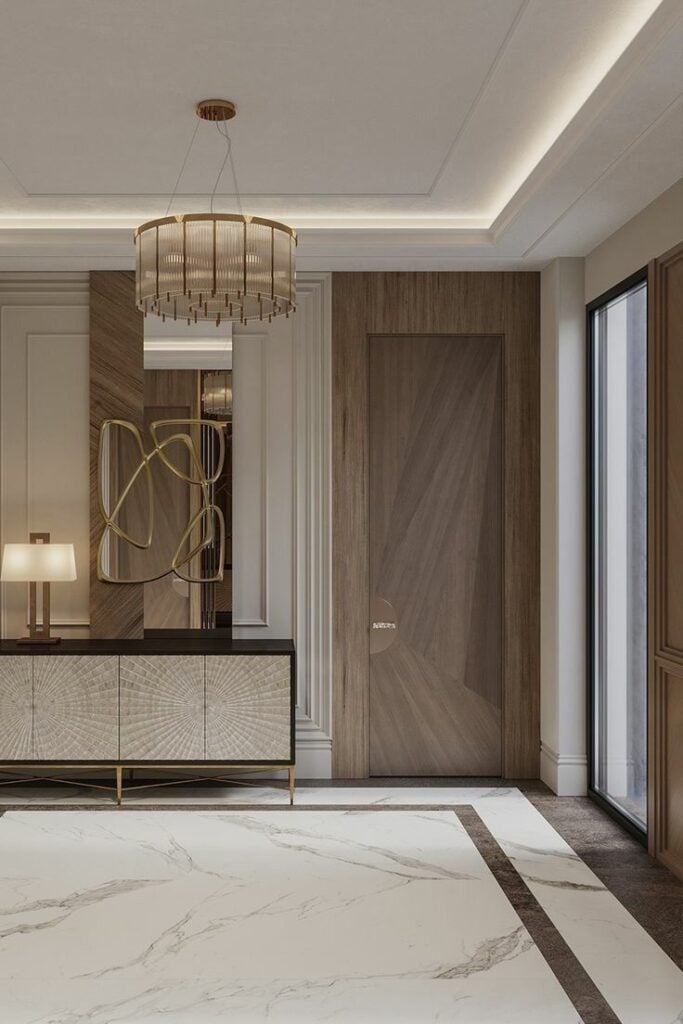 Luxury modern foyer with marble floors, wood-paneled door, decorative console table, sculptural mirror and gold chandelier, ceiling lighting