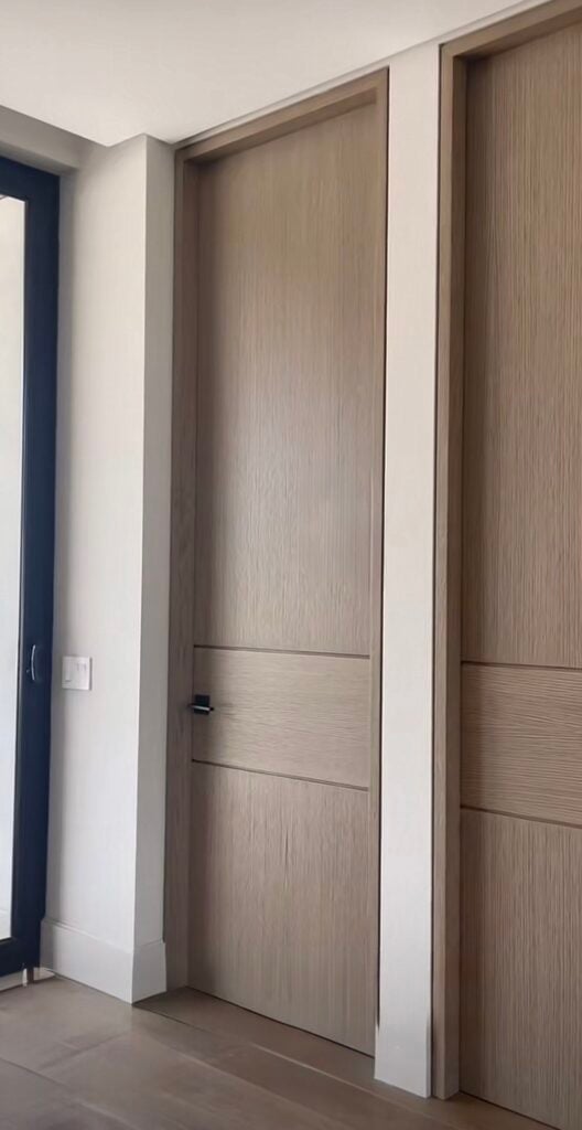 Contemporary hallway with flush light oak interior doors, black lever handle, white trim and natural hardwood flooring.