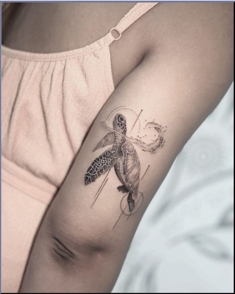Sea turtle tattoo on inner upper arm, fine-line black and gray design with geometric lines and water splash, model wearing pale pink top