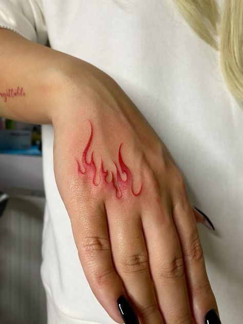 Close-up of a woman's hand with a minimalist red flame tattoo on the back of the hand and black nails