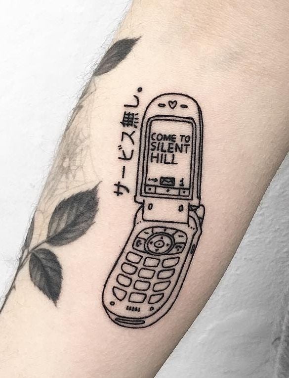 Blackwork forearm tattoo of a retro flip phone showing COME TO SILENT HILL, with vertical Japanese text and leaf illustrations.