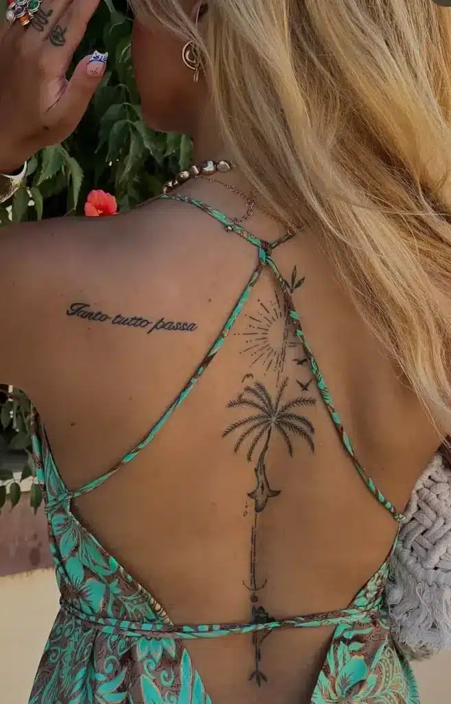 Back view of woman in green strappy dress displaying spine palm tree tattoo, sun, birds and script Tanto tutto passa.
