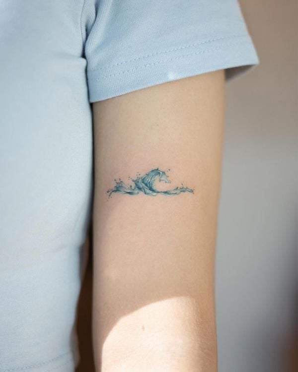 Close-up of small minimalist blue wave tattoo on inner upper arm, ocean-inspired ink art on light skin, minimal tattoo design.