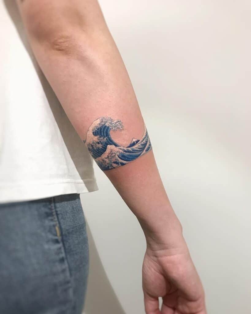 Hokusai Great Wave forearm band tattoo in blue ink wrapped around inner forearm