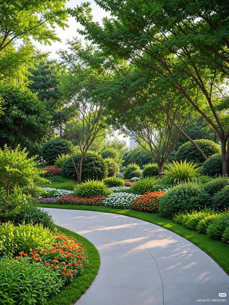 Curved concrete path winding through a lush landscaped garden with flowering beds, trimmed shrubs, and shady trees in a park-like setting.