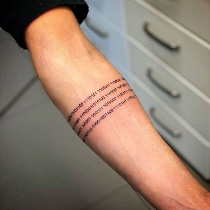 Close-up of forearm with tech-inspired black binary code armband tattoo (rows of 0s and 1s) wrapping around the lower arm.