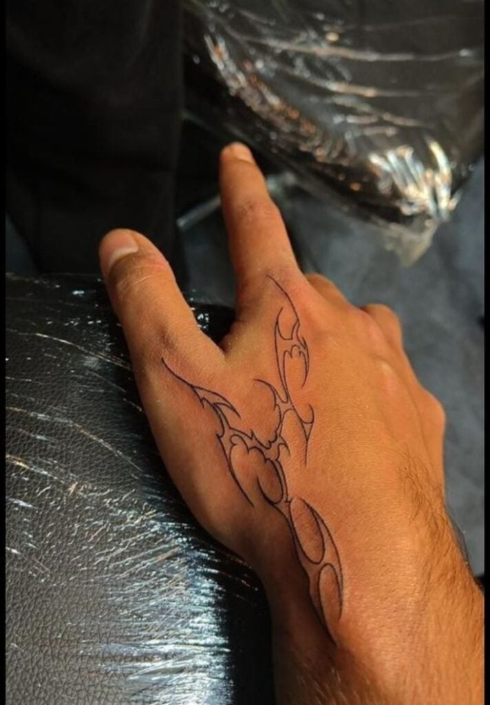 Close-up hand with black tribal-outline tattoo from index finger across back of hand, minimal finger tattoo idea.