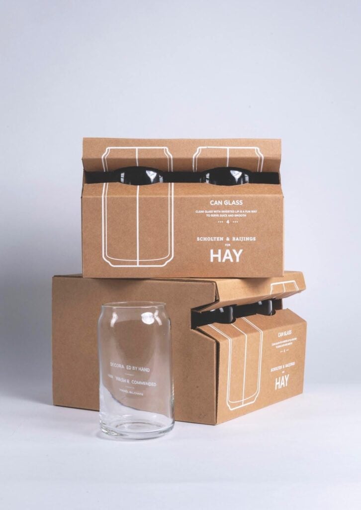 HAY Can Glass: clear can-shaped drinking glass with stacked brown HAY packaging boxes — minimalist product shot