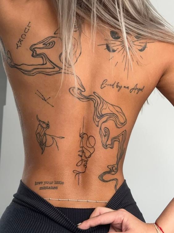 Woman's tattooed back featuring fine-line abstract swirls, minimalist face and bull sketches, and script 'loved by my Angel'.