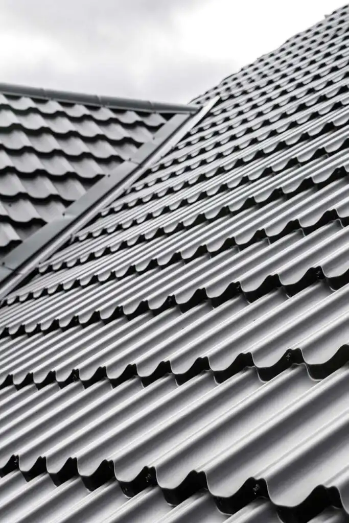 Dark gray corrugated metal roof tiles, close-up diagonal view showing repeating wavy pattern and overlapping modern roofing panels.