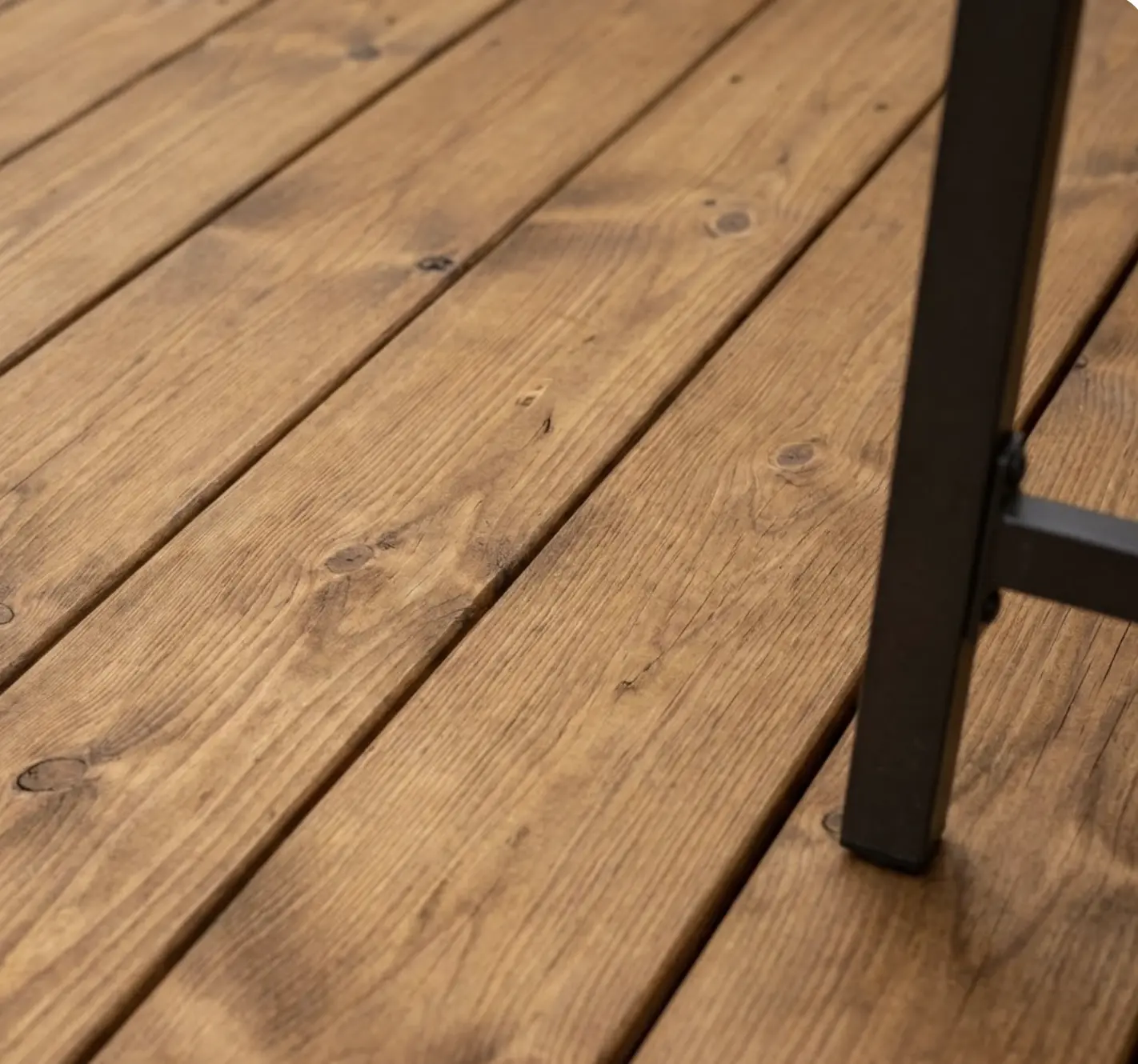 Close-up of stained wooden deck boards with knots and grain texture, black metal chair leg on outdoor patio flooring
