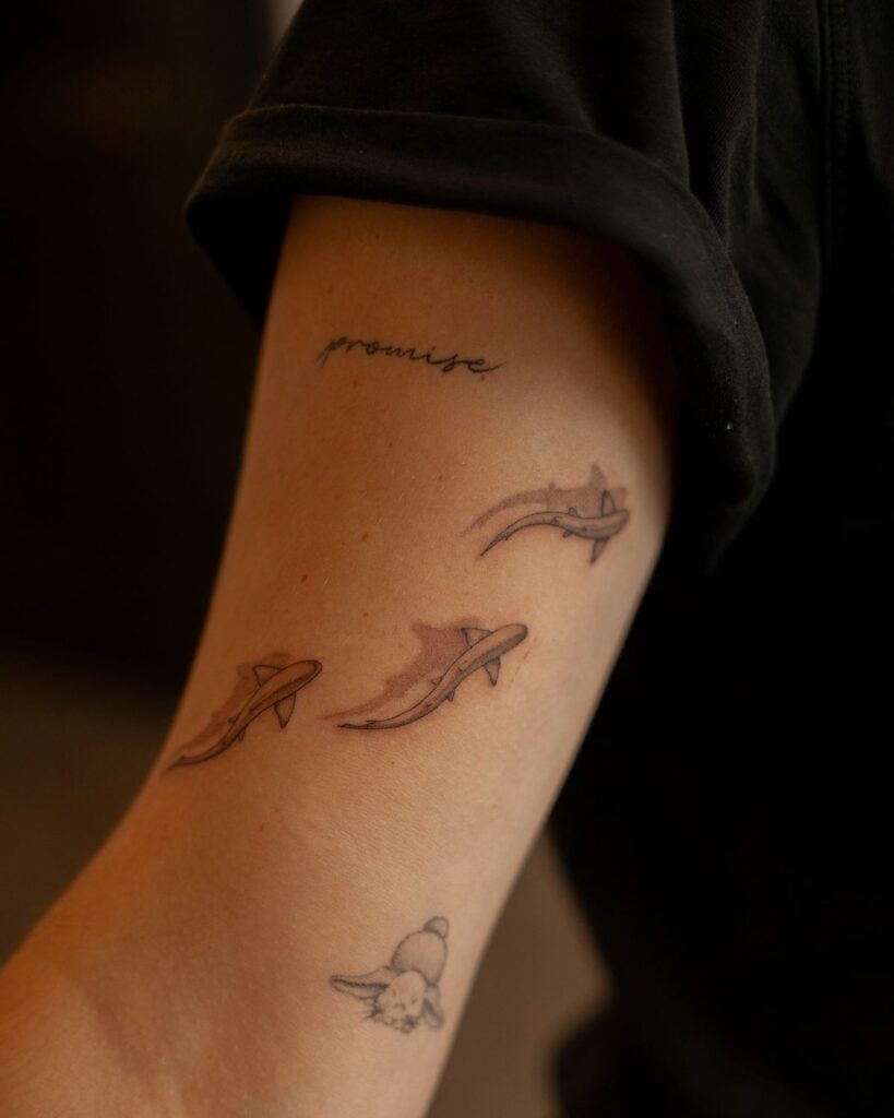 Arm tattoos: close-up of inner forearm with three minimalist shark designs, small rabbit sketch and cursive 'promise' word