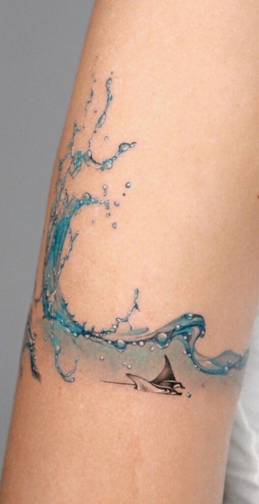 Water splash forearm tattoo with blue droplets and a small manta ray — realistic ocean-inspired arm tattoo design