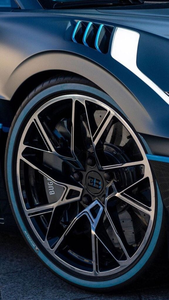 Close-up of Bugatti alloy wheel and low-profile tire with blue accent stripe, intricate multi-spoke rim and sporty fender vent detail.