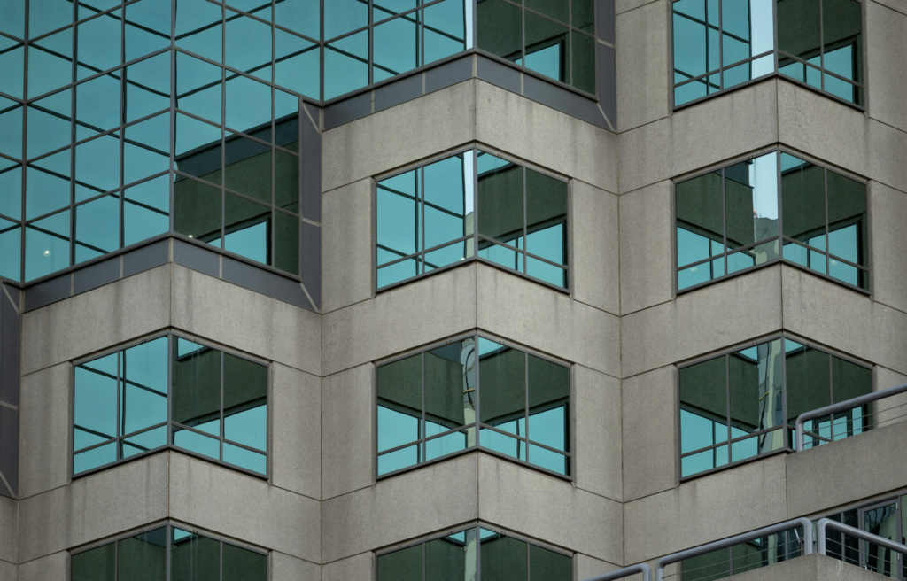 Screenshot 2026-02-27 at 165500 Modern office building facade with repeating angular bay windows and teal reflective glass. | Sky Rye Design Modern office building facade with repeating angular bay windows and teal reflective glass.
