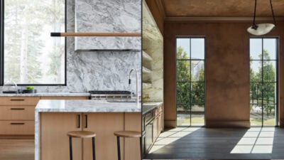 Modern kitchen with marble countertops, wood cabinets and breakfast bar stools, flooded with natural light from tall windows overlooking a garden.