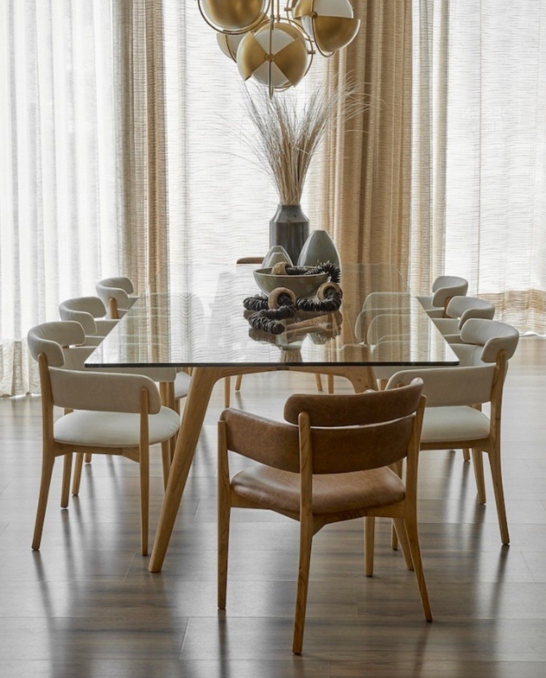 Modern minimalist dining room interior with glass-top table, wooden mid-century chairs, neutral palette and pendant light.