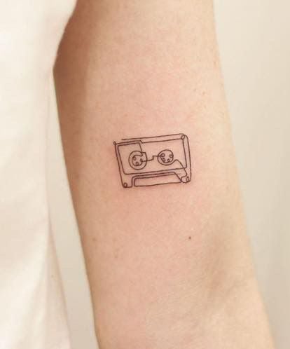 Minimalist black-ink cassette tape tattoo on inner forearm — small retro music linework, simple outline design.