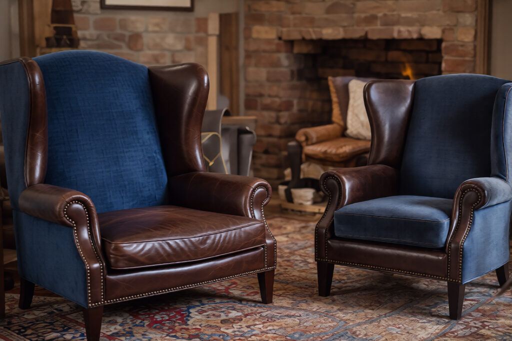 3 1 Blue velvet and brown leather wingback chairs in cozy living room with brick fireplace and patterned rug | Sky Rye Design Blue velvet and brown leather wingback chairs in cozy living room with brick fireplace and patterned rug