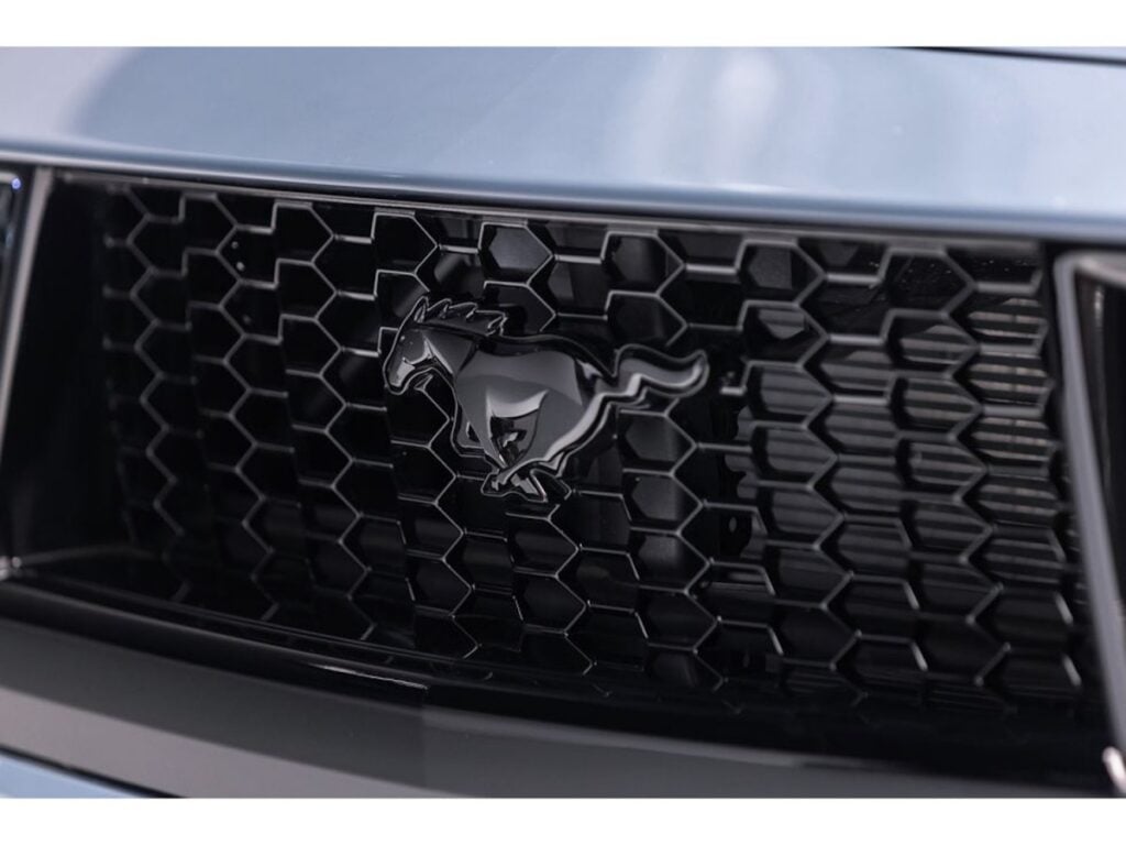 Close-up of black Ford Mustang pony emblem on honeycomb front grille, sleek black finish automotive detail for muscle car marketing