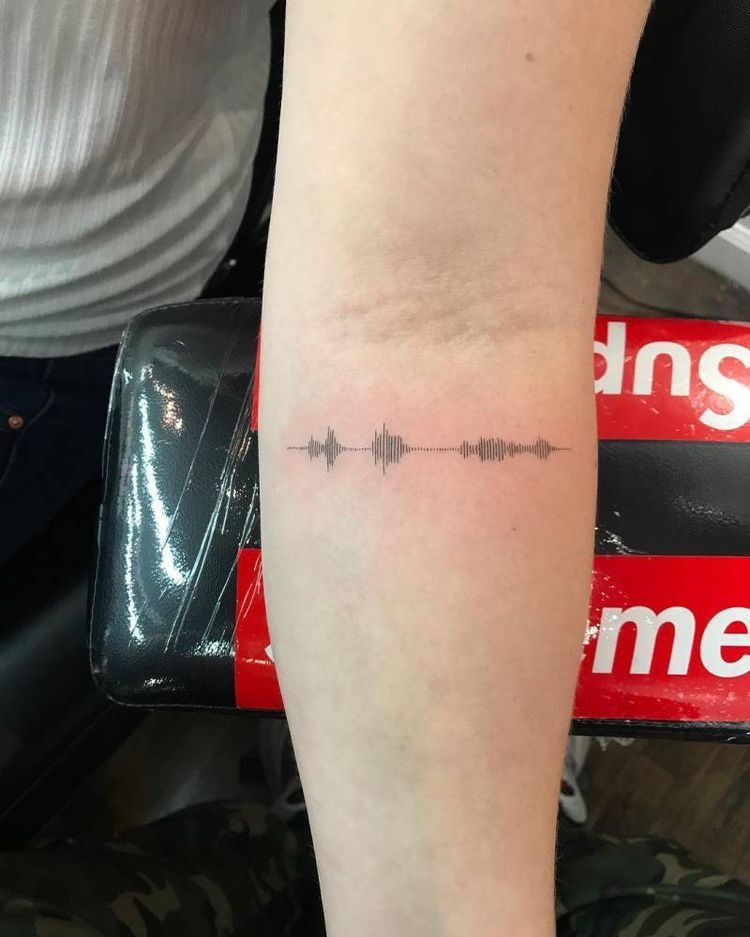 Minimal black soundwave tattoo design on inner forearm, close-up modern audio waveform ink