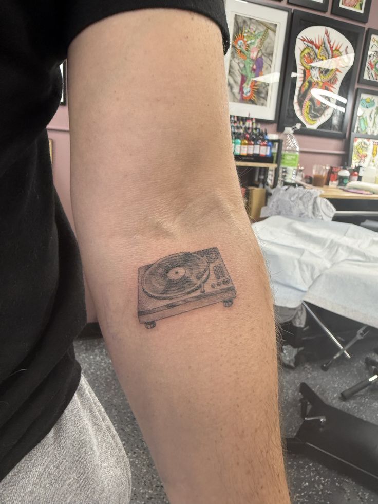 Close-up of forearm tattoo of a vintage vinyl record turntable in black ink, tattoo studio backdrop