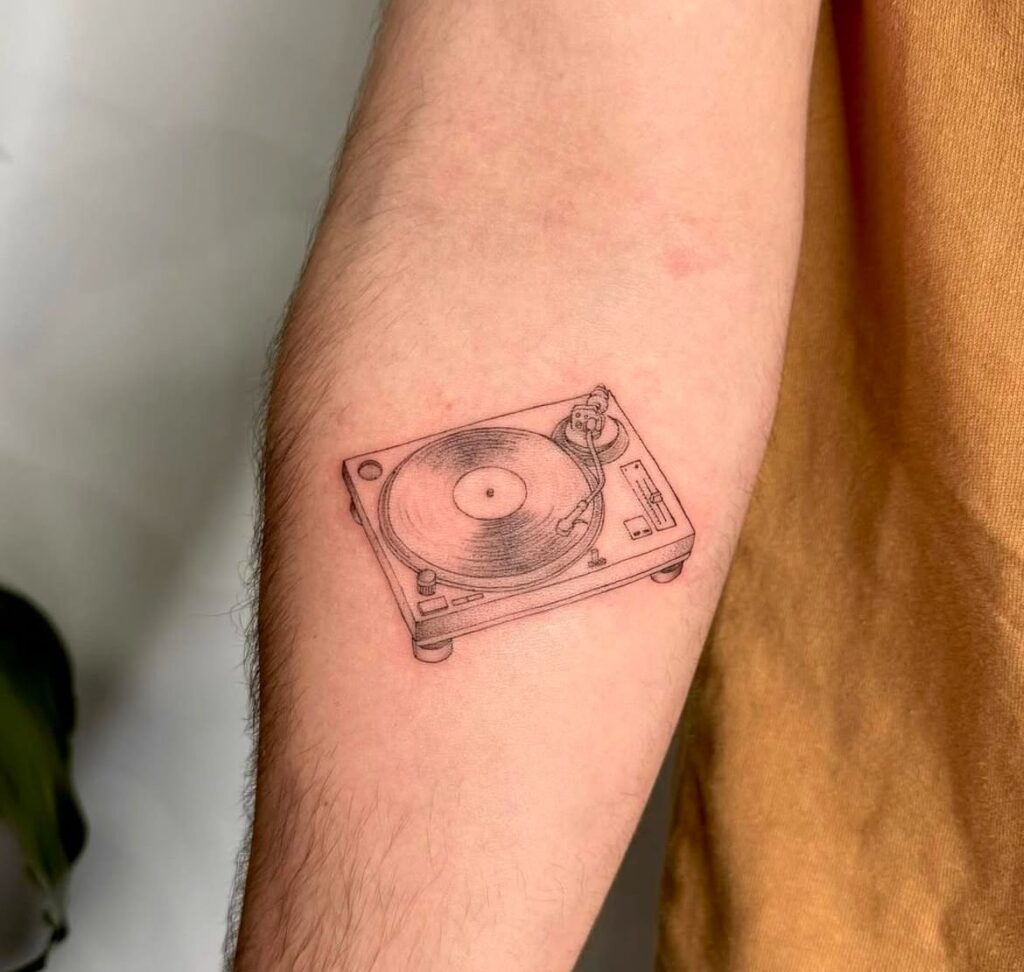 Small fine-line forearm tattoo of a vintage turntable with vinyl record, minimal black-ink music tattoo.