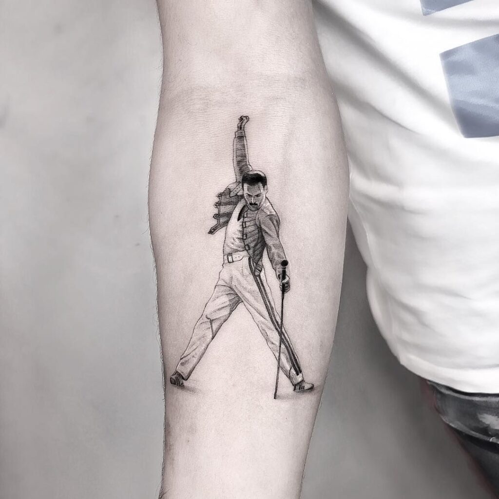 Black and gray forearm tattoo of a male singer in triumphant pose with raised fist and microphone stand, detailed linework