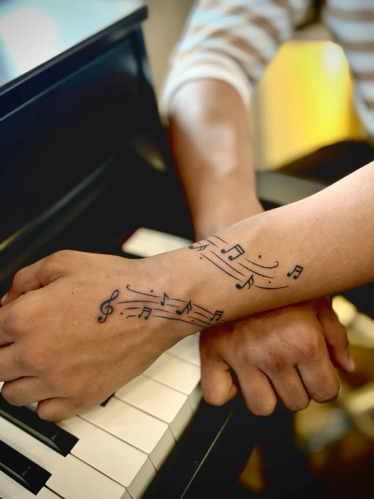 Close-up of a musician's hands with musical notes forearm tattoos on piano keys