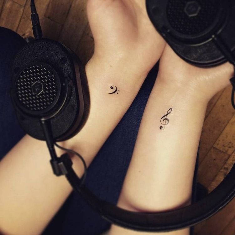 Minimal treble clef and bass clef wrist tattoos beside black over-ear headphones, small music-themed wrist tattoos
