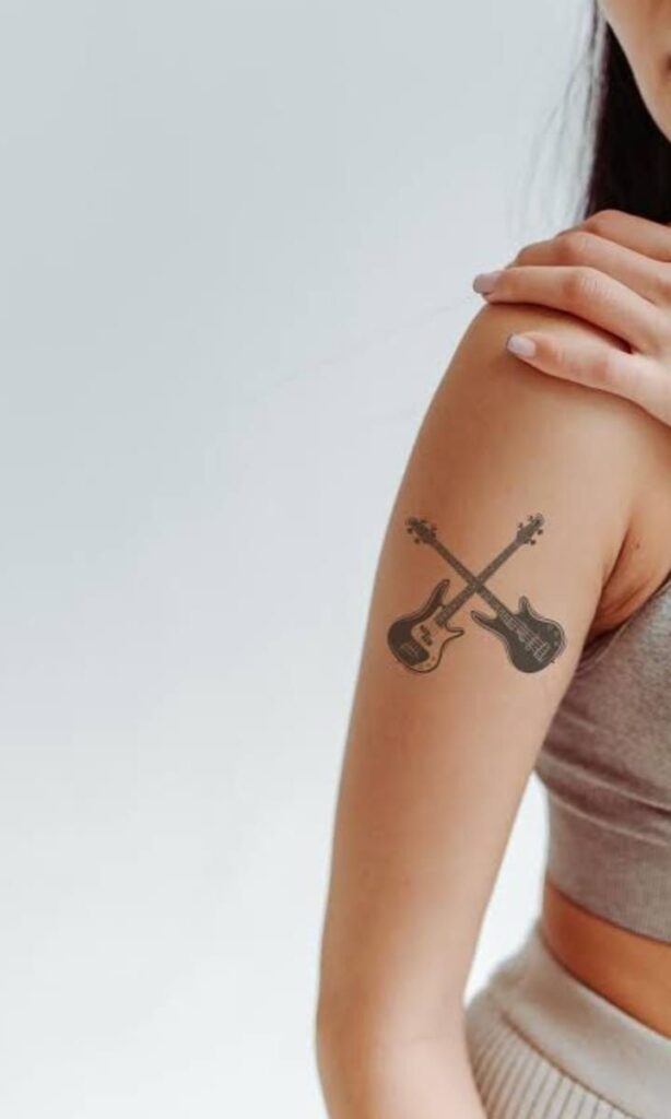 Close-up of woman's upper arm showing crossed electric guitar music tattoo design