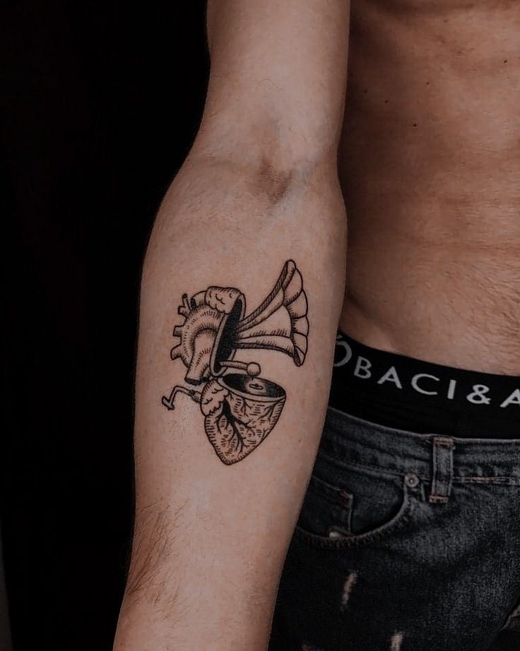 Anatomical heart gramophone tattoo on forearm, black-ink vintage phonograph horn, music-themed body art