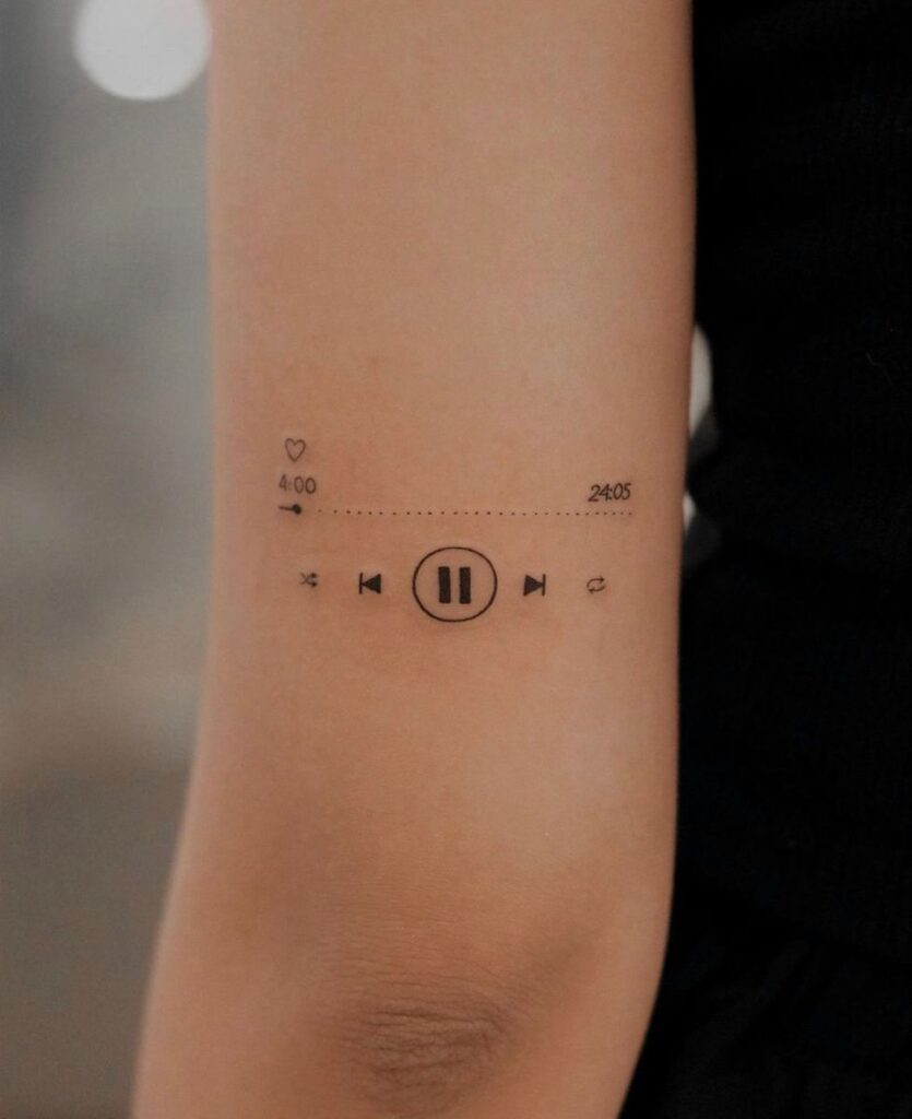 Minimalist music player tattoo on inner forearm showing play/pause, skip, shuffle icons and progress bar with timestamps