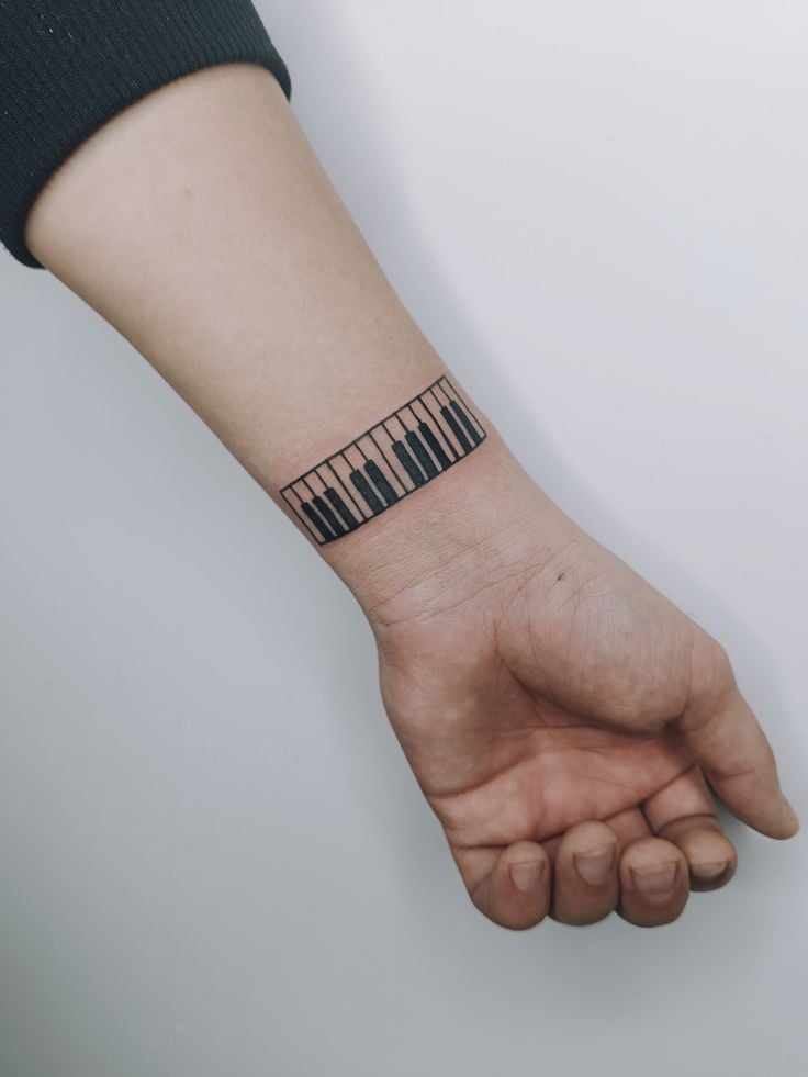 Piano keyboard armband tattoo on inner wrist and forearm, minimalist black keys design