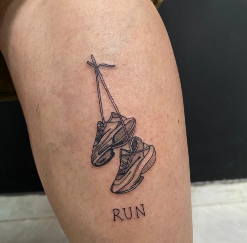 Minimalist black linework calf tattoo of hanging running shoes with RUN text, athletic sneaker design