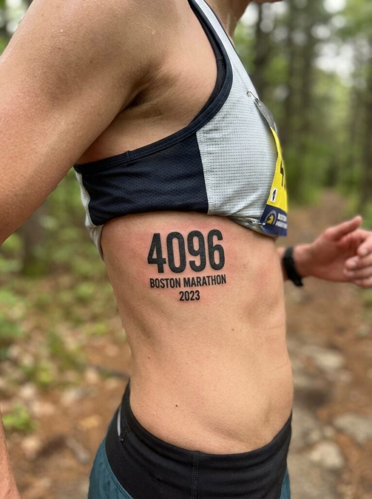 Runner's side with bold 4096 Boston Marathon 2023 tattoo on ribcage, wearing race top and watch on trail