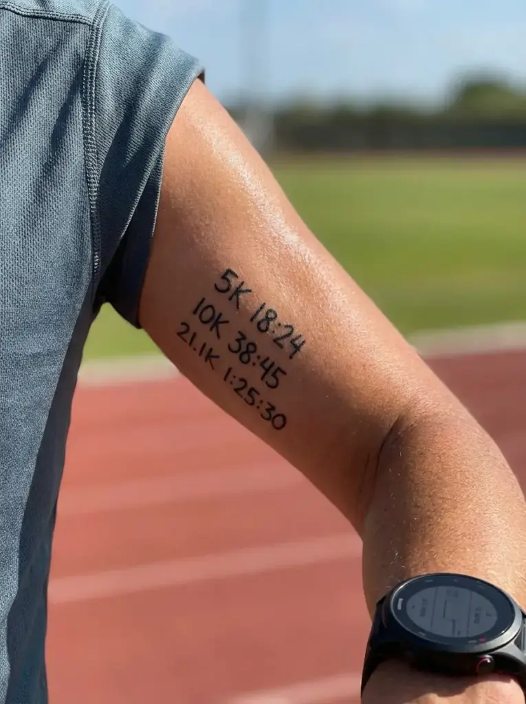 Runner's forearm tattoo listing race times (5K 18:24, 10K 38:45, 21.1K 1:25:30) with GPS watch on track
