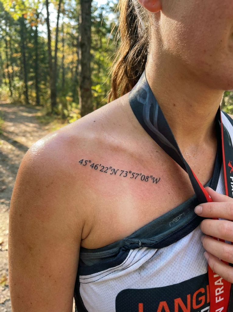 Coordinates tattoo on collarbone 45°46'22N 73°57'08W on female runner wearing race medal in forest