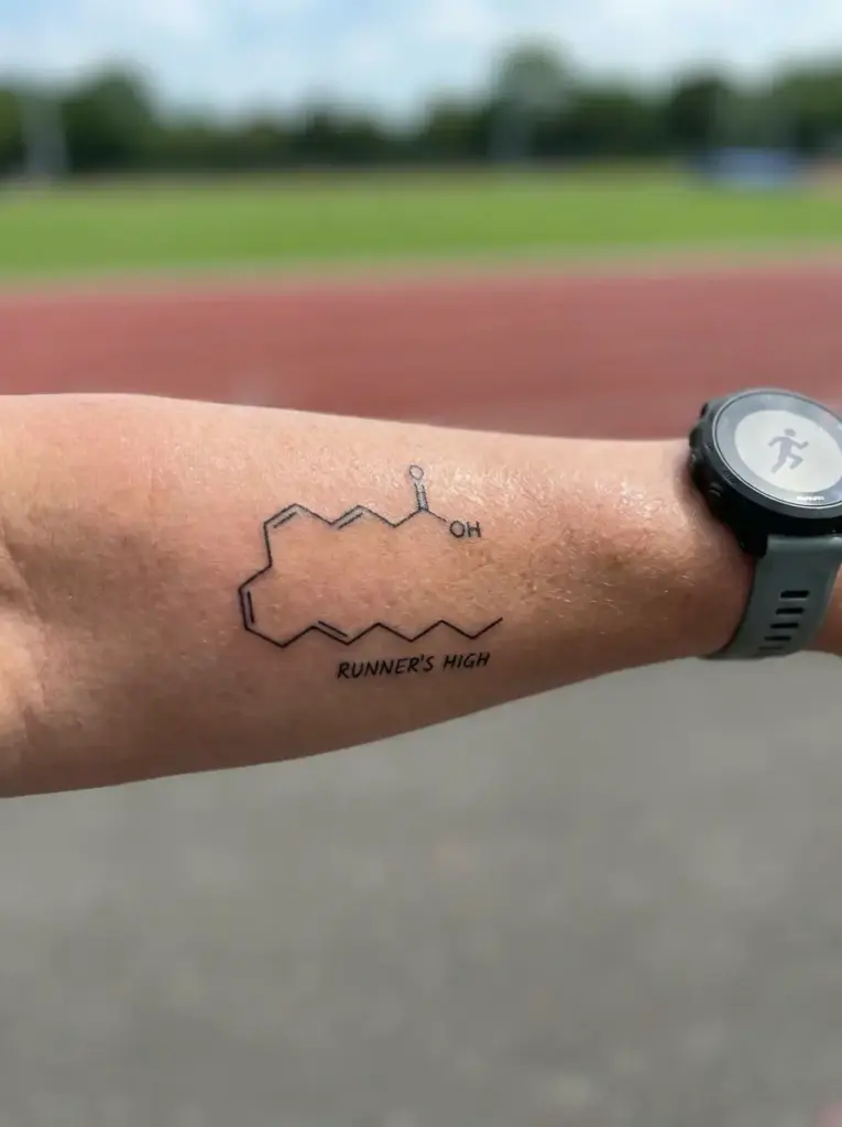 Runner's High tattoo - endorphin molecule on forearm beside running watch, blurred track in background