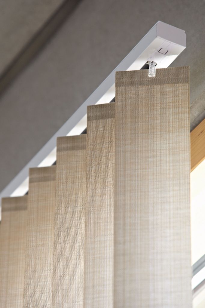 Beige textured vertical fabric blinds on a white track, modern sliding panel curtains filtering sunlight