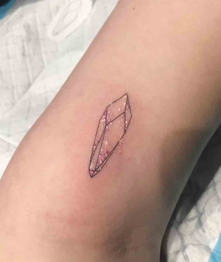 Small geometric crystal tattoo with pink watercolor fill and tiny white star highlights, fine-line black outline on skin.