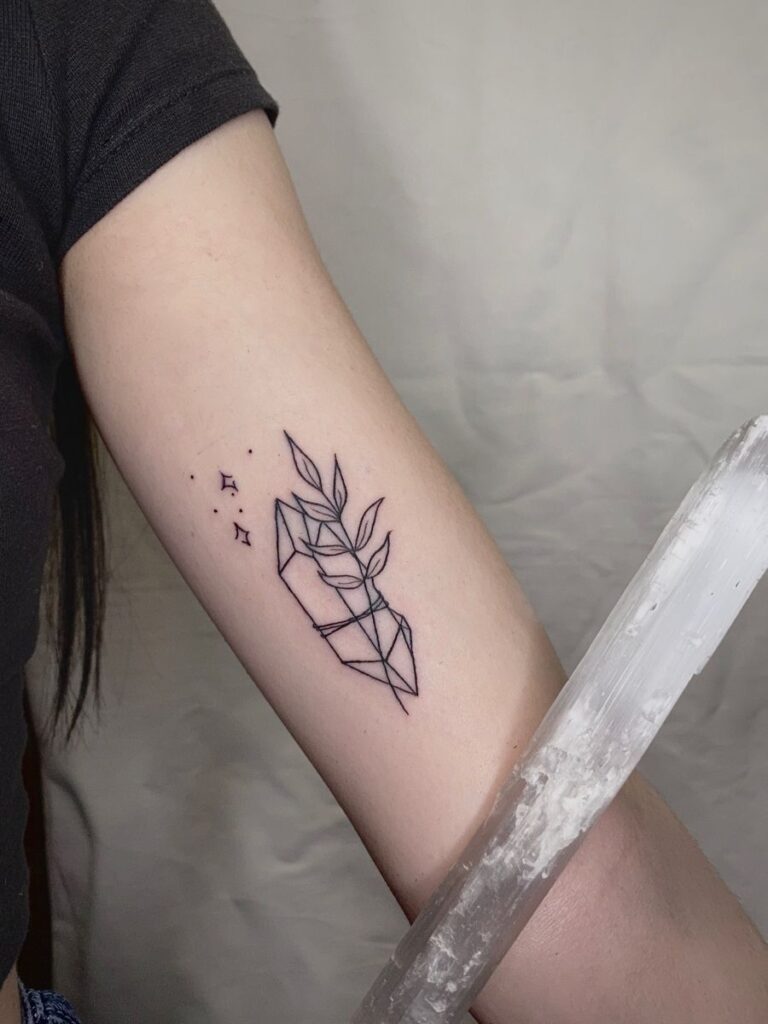 Minimalist linework forearm tattoo of a geometric crystal entwined with botanical leaves and small star accents