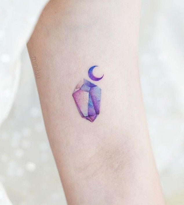 Small purple watercolor crystal tattoo with crescent moon on inner forearm, minimalist ink