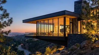 Modern luxury cantilever glass house on hillside with interior lights and panoramic valley views at sunset