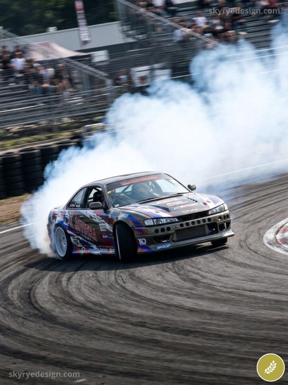 Modified drift car sliding on racetrack, producing thick smoke and tire marks at a spectator motorsport event