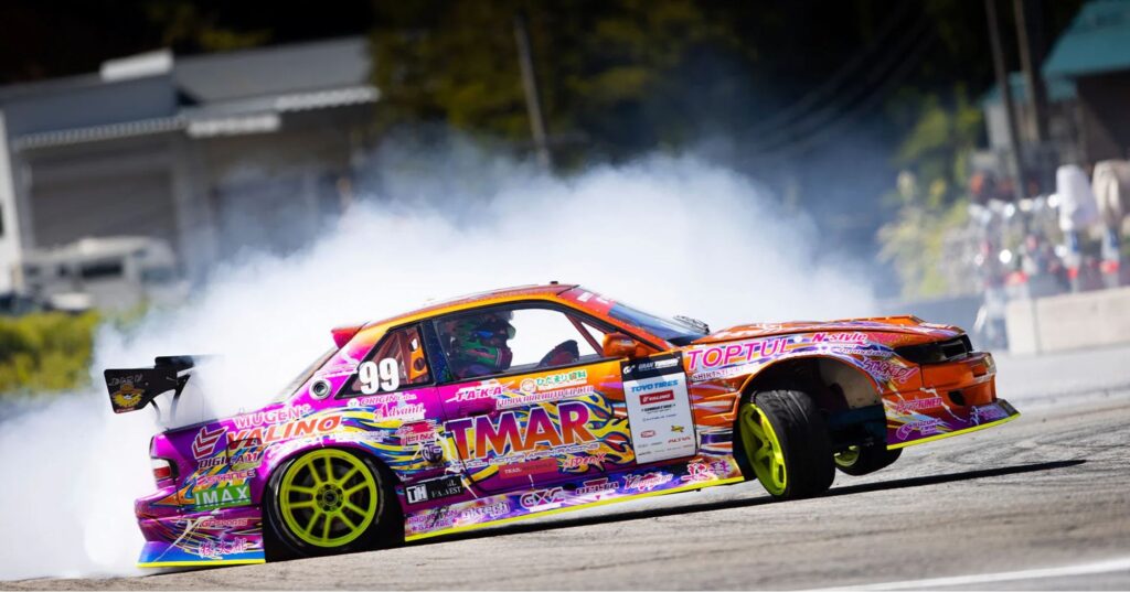 Colorful drift car with neon green wheels sliding sideways, leaving thick white tire smoke during a motorsport drift event